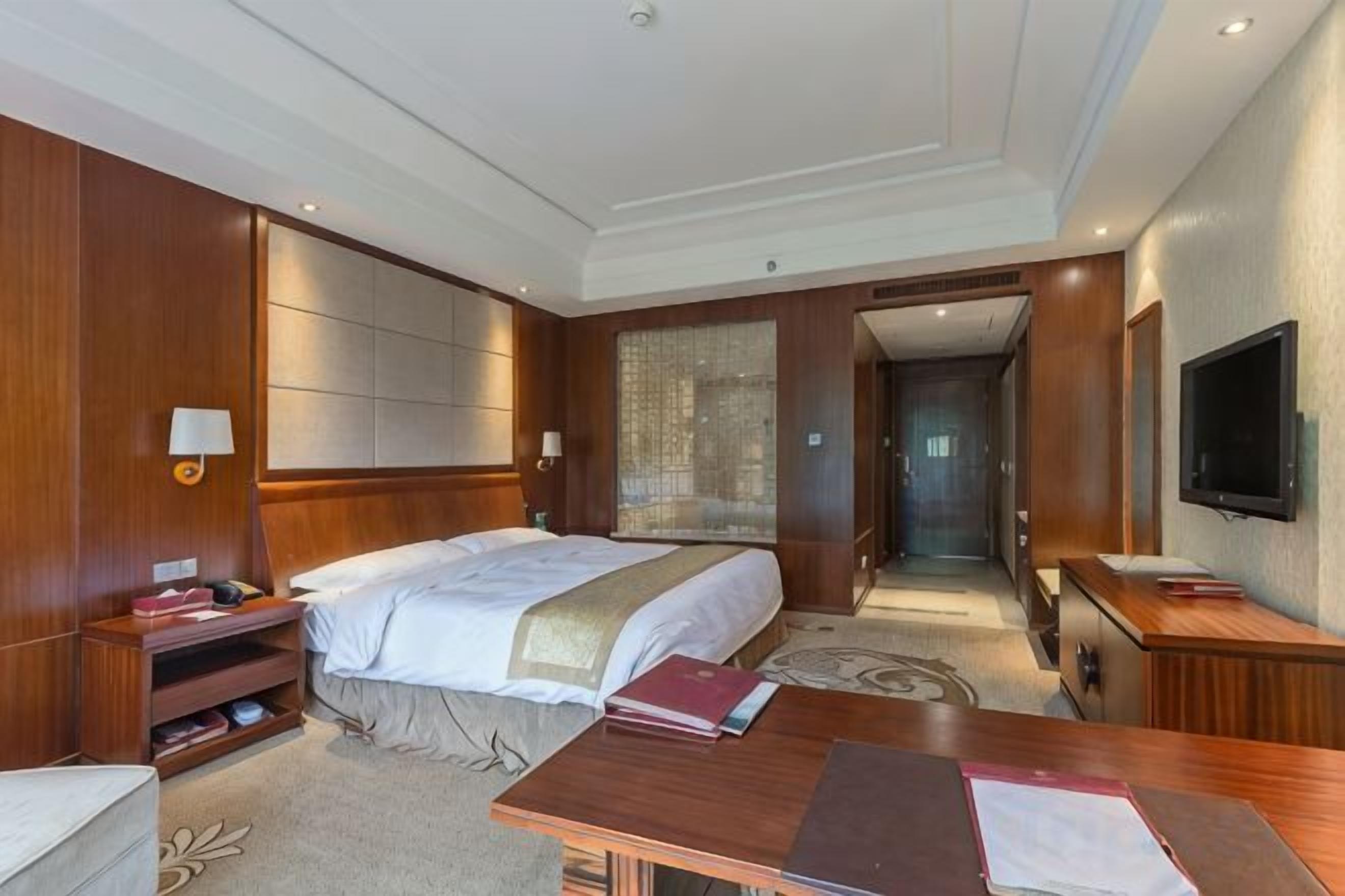 A hotel room with a large bed, bedside tables, a desk, a flat-screen TV, and a walk-in closet.