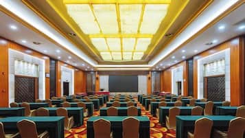 Un salón de conferencias con filas de mesas y sillas, una pantalla grande al frente y una alfombra estampada.