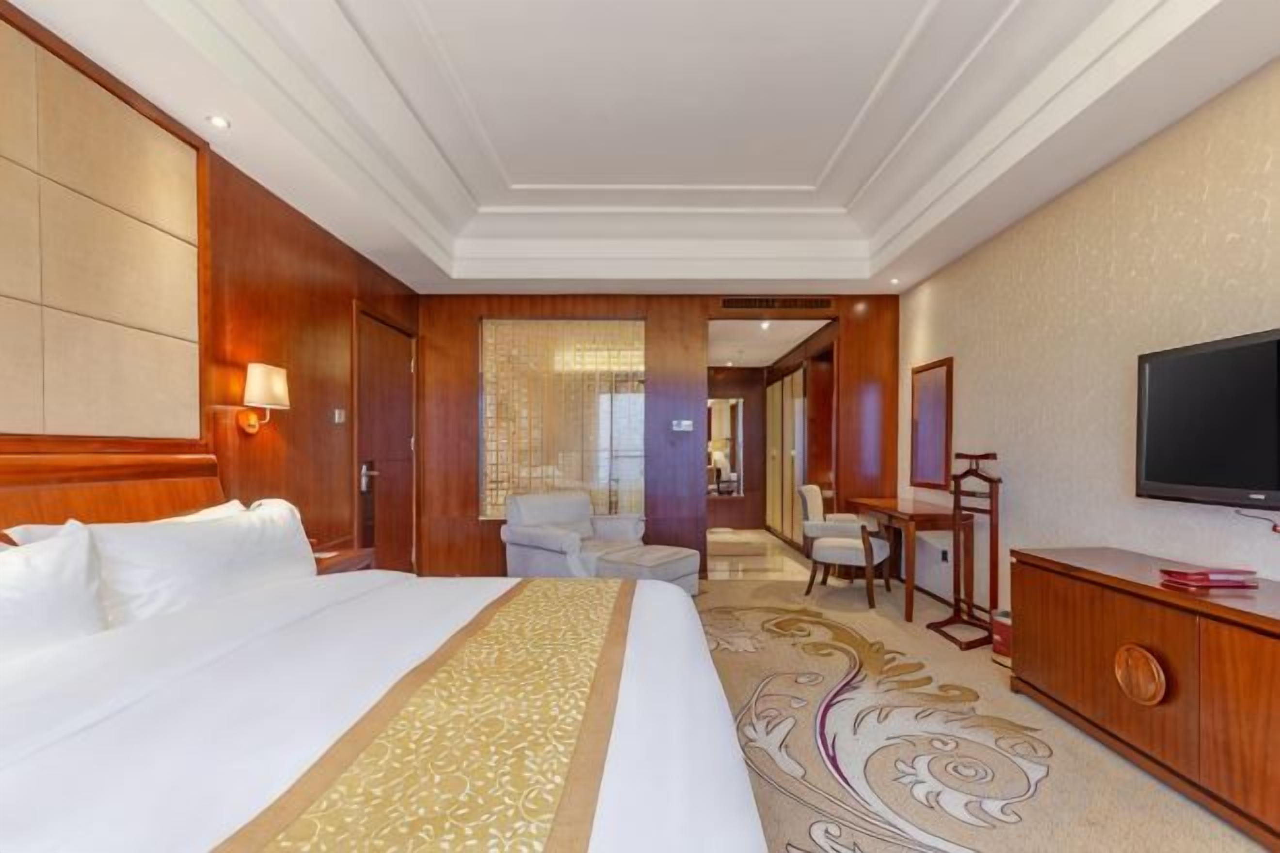 A hotel room with a large bed, a television, a desk, and a chair.