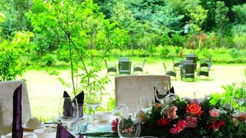 An outdoor dining area with tables set for two, surrounded by lush greenery.