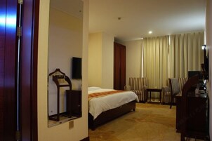 Una habitación de hotel con cama, escritorio, silla, televisor y ventana con cortinas.