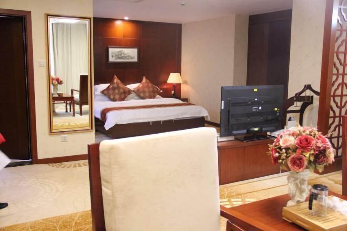 Habitación de hotel con una cama, televisor, escritorio con un florero y un espejo.