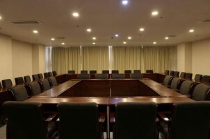 Un salón de conferencias con una larga mesa y sillas, ventanas grandes con cortinas e iluminación empotrada en el techo.