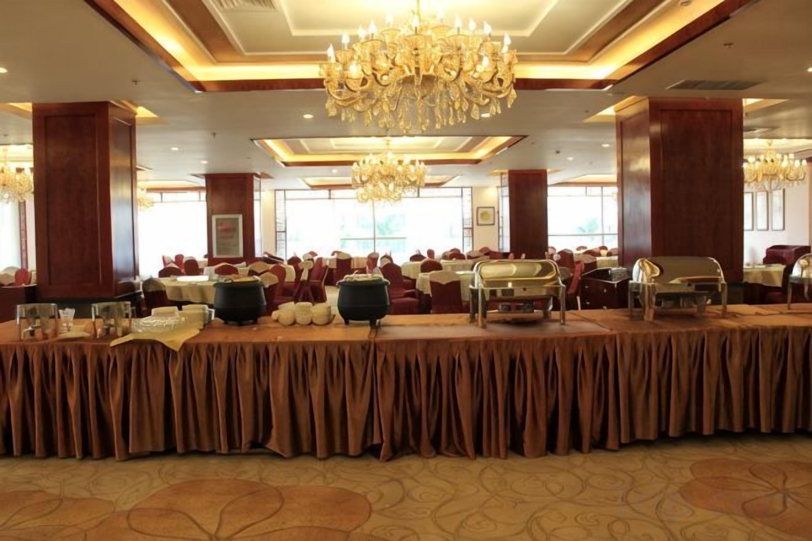 A banquet hall with a long table, chandeliers, and red chairs.