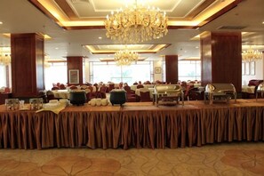 Un salón de banquetes con una larga mesa, candelabros y sillas rojas.