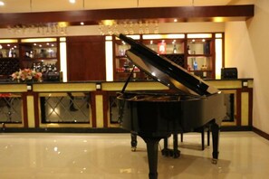 Un piano de cola en un vestíbulo amplio, con una zona de bar al fondo.