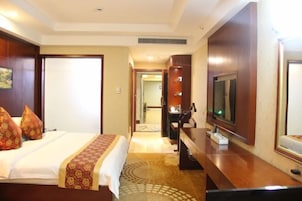 Una habitación de hotel con una cama, un escritorio, un televisor y un espejo.
