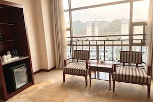 Una habitación con una mesa de comedor, dos sillas a rayas, un minibar y un ventanal con vistas a edificios y colinas.