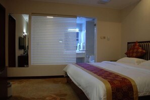 Una habitación de hotel con cama, ventana con persianas, espejo y un pequeño escritorio.