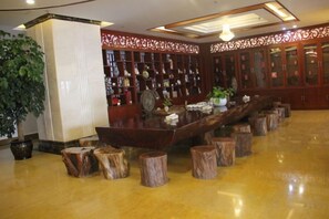 A lobby with a long wooden reception desk, a large potted plant, and a wall of bookshelves. - an Ran Hotel (Zhenkang)