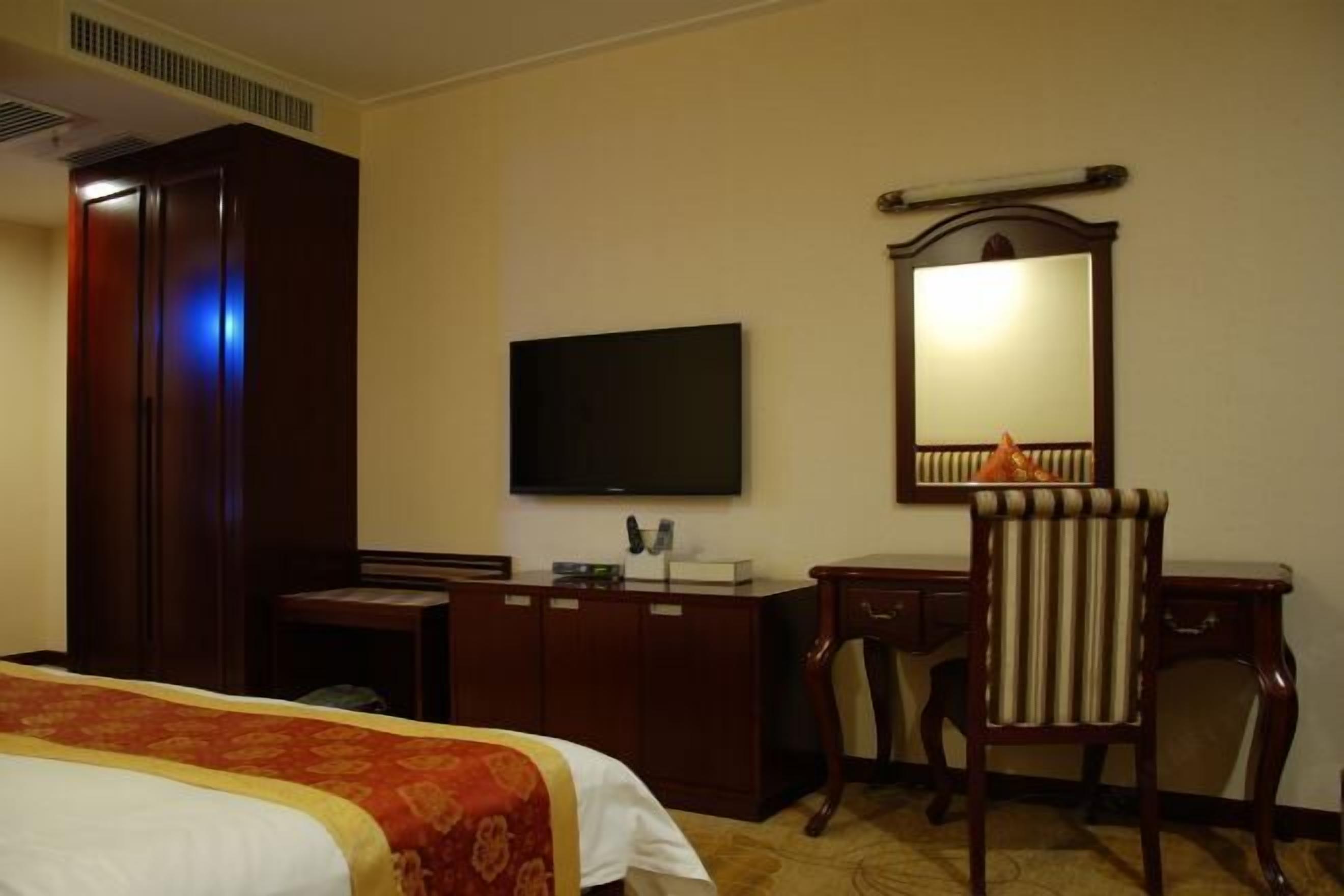 A hotel room with a bed, a desk, a television, a mirror, and a chair.