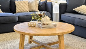 A modern living room with a dark grey sofa, a round wooden coffee table, and a decorative vase with flowers. - Serenity by the Bay - Whole House in Vincentia, Jervis Bay (Vincentia)