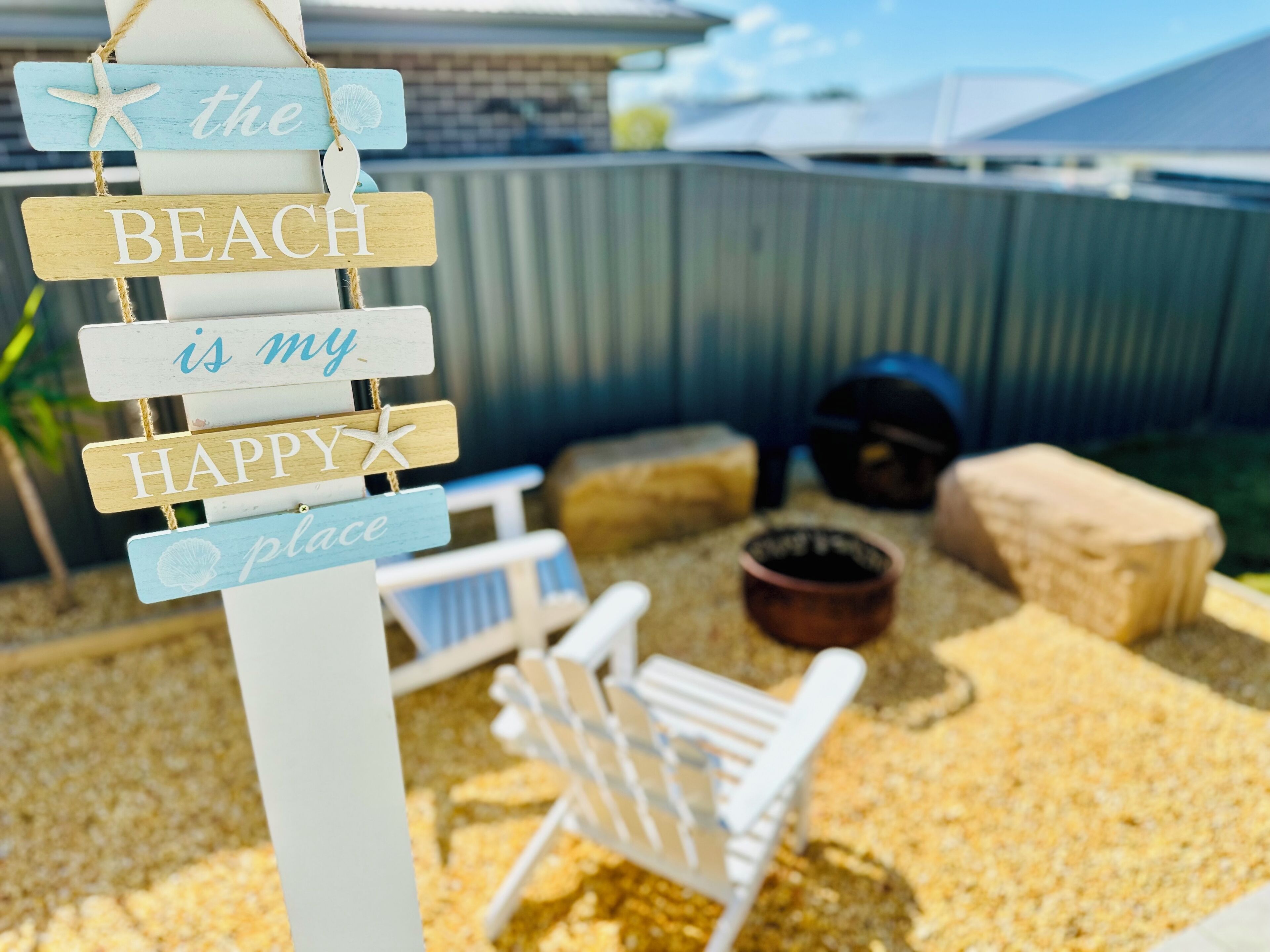 A wooden sign with the text "the BEACH is my HAPPY place" in a backyard setting.