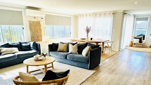 A spacious living room with a dark blue sofa, a round wooden coffee table, and a wicker chair. - Serenity by the Bay - Whole House in Vincentia, Jervis Bay (Vincentia)