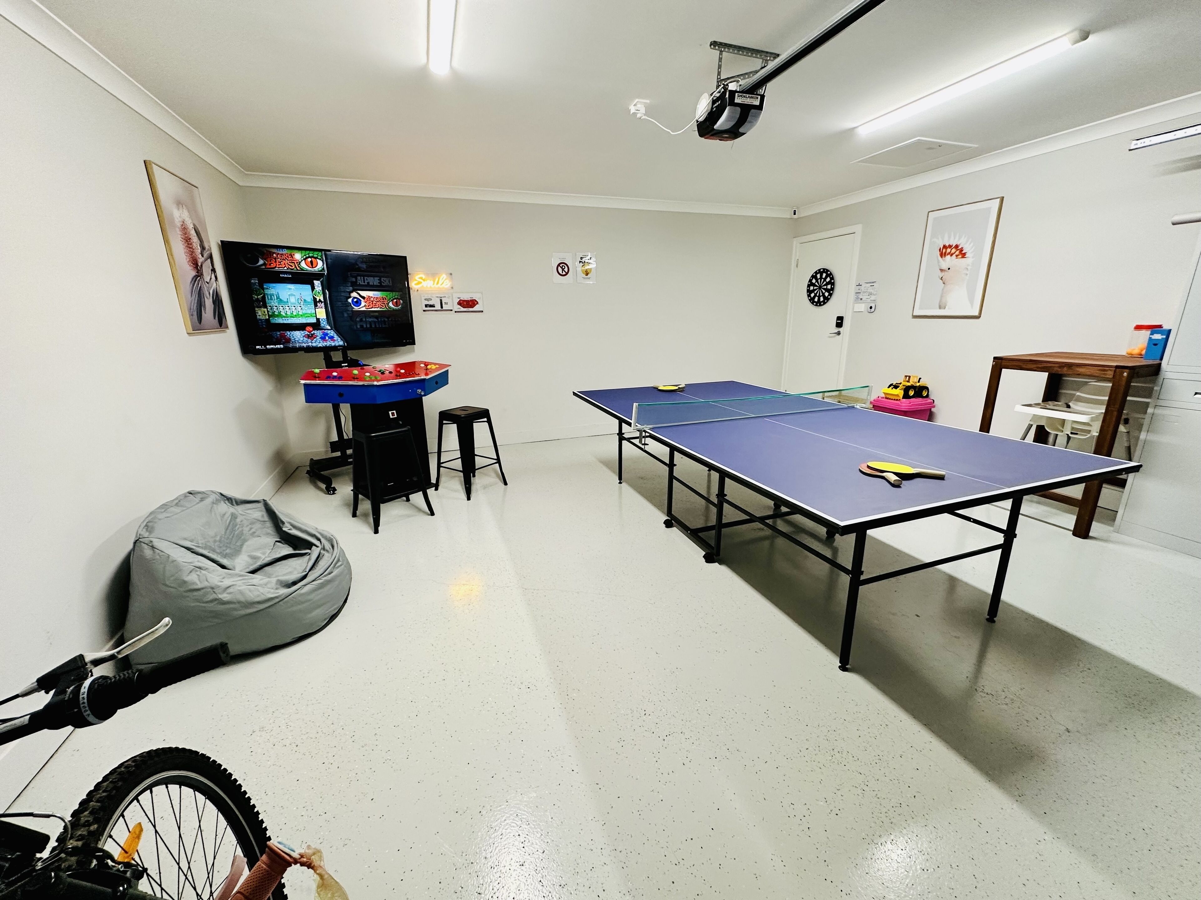 Um quarto com mesa de pingue-pongue, televisão, puff e bicicleta.
