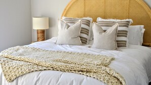 A bed with a woven headboard, striped pillows, and a chunky knit blanket. - Serenity by the Bay - Whole House in Vincentia, Jervis Bay (Vincentia)