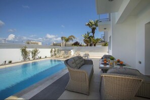 A rooftop pool area with wicker furniture, a table with drinks, and a view of the cityscape. - Villa Marina in Pernera (Paralimni)