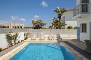 A rooftop pool with lounge chairs, surrounded by palm trees and a view of buildings. - Villa Marina in Pernera (Paralimni)