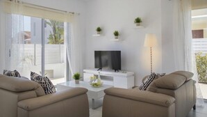 Una sala de estar moderna con un televisor de pantalla plana, dos sofás color beige, una mesa de centro y una lámpara de pie.