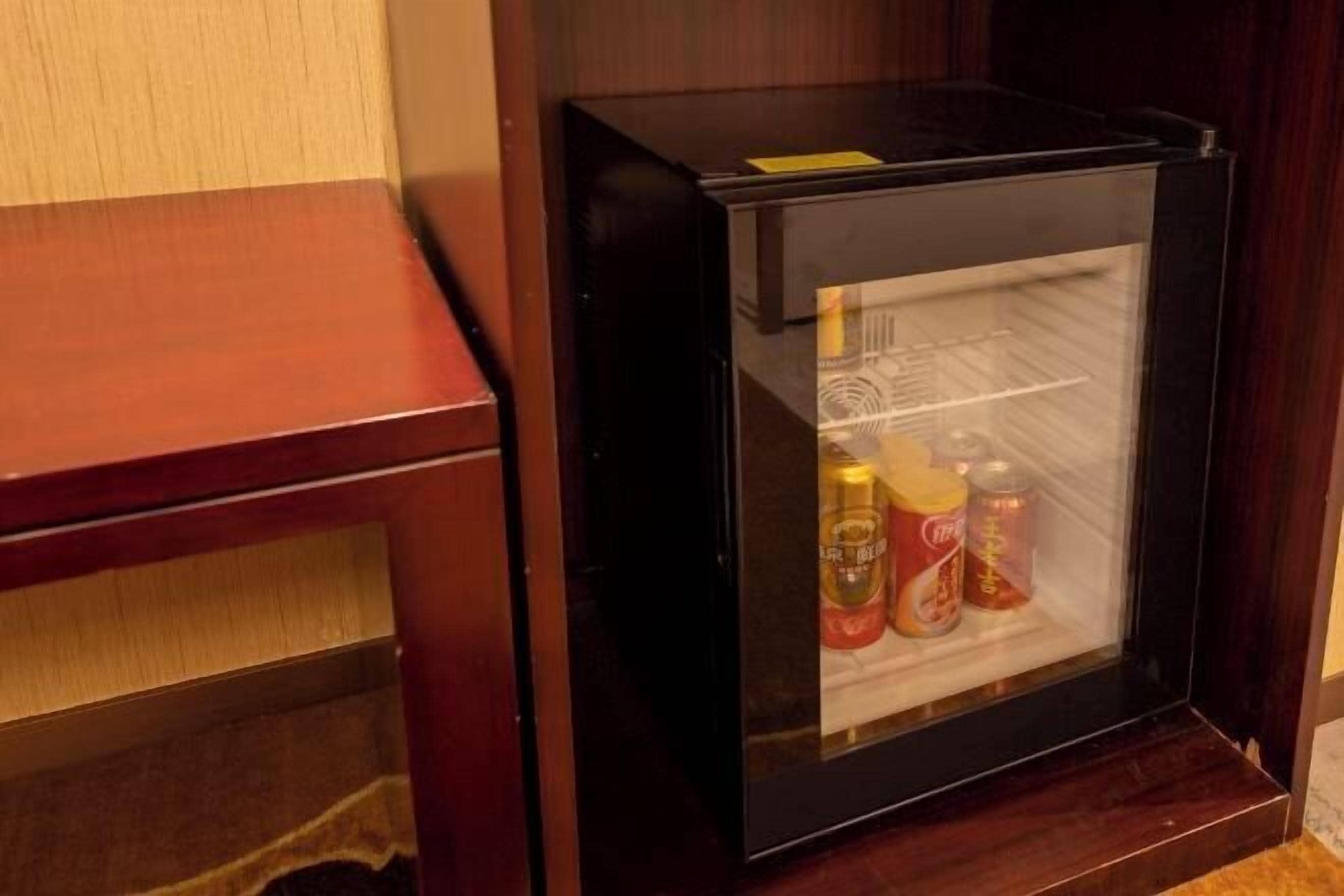Geladeira compacta com porta de vidro, contendo bebidas e acompanhamentos.