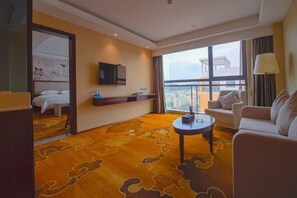 Une chambre d’hôtel avec une grande fenêtre, un canapé, une table basse et un téléviseur fixé au mur.