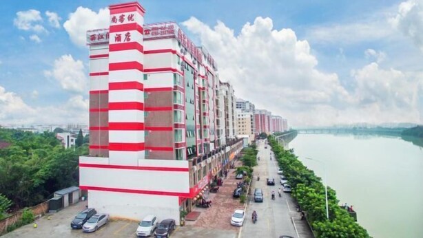 A multi-story hotel with a red and white facade, located beside a river. - Shankee Express Hotel (Meizhou Lijiangwan) (Meizhou)