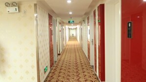 A hotel corridor with patterned carpet, red and white walls, and an emergency exit sign. - Shankee Express Hotel (Meizhou Lijiangwan) (Meizhou)
