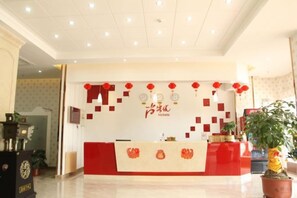 A hotel reception area with a red and white color scheme, a reception desk, and a potted plant. - Shankee Express Hotel (Meizhou Lijiangwan) (Meizhou)