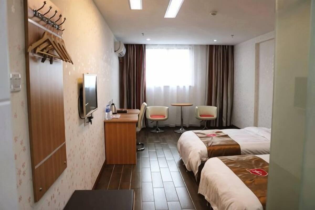 A hotel room with a bed, desk, chairs, and a TV.