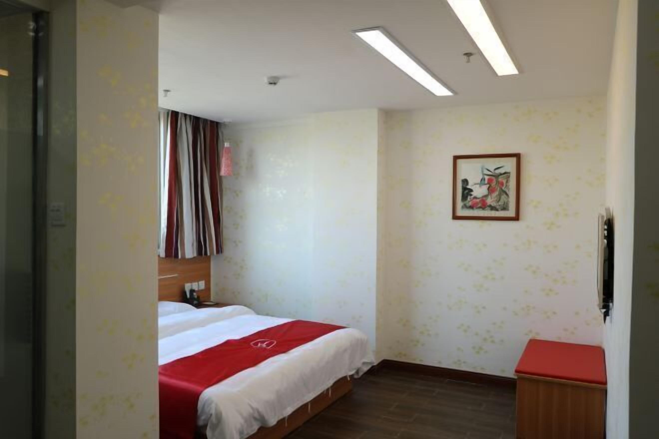 Una habitación de hotel con una cama, un pequeño armario de madera, un cuadro en la pared y una ventana con cortinas.