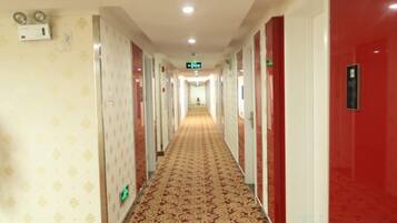 A hotel corridor with a patterned carpet, doors on both sides, and a green exit sign.