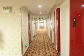 A hotel corridor with a patterned carpet, doors on both sides, and a green exit sign. - Shankee Express Hotel (Meizhou Lijiangwan) (Meizhou)