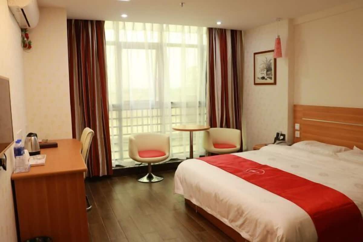 A hotel room with a bed, a desk, two chairs, a small table, and a window with curtains.