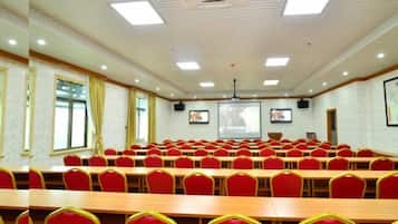Un salón de conferencias con hileras de sillas rojas, una mesa grande y una pantalla para proyector.