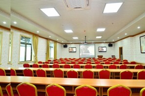 Un salón de conferencias con hileras de sillas rojas, una mesa grande y una pantalla para proyector.
