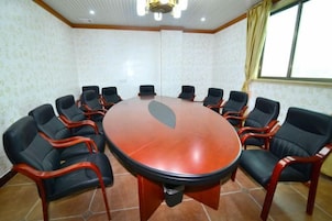 Un salón de conferencias con una mesa redonda rodeada de sillas, suelo de baldosas y una ventana con cortinas.