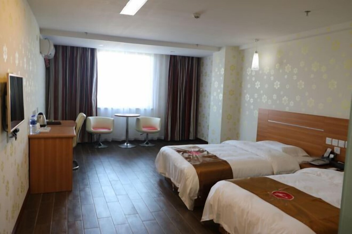 A hotel room with two beds, a desk, a chair, a small table, and a TV.