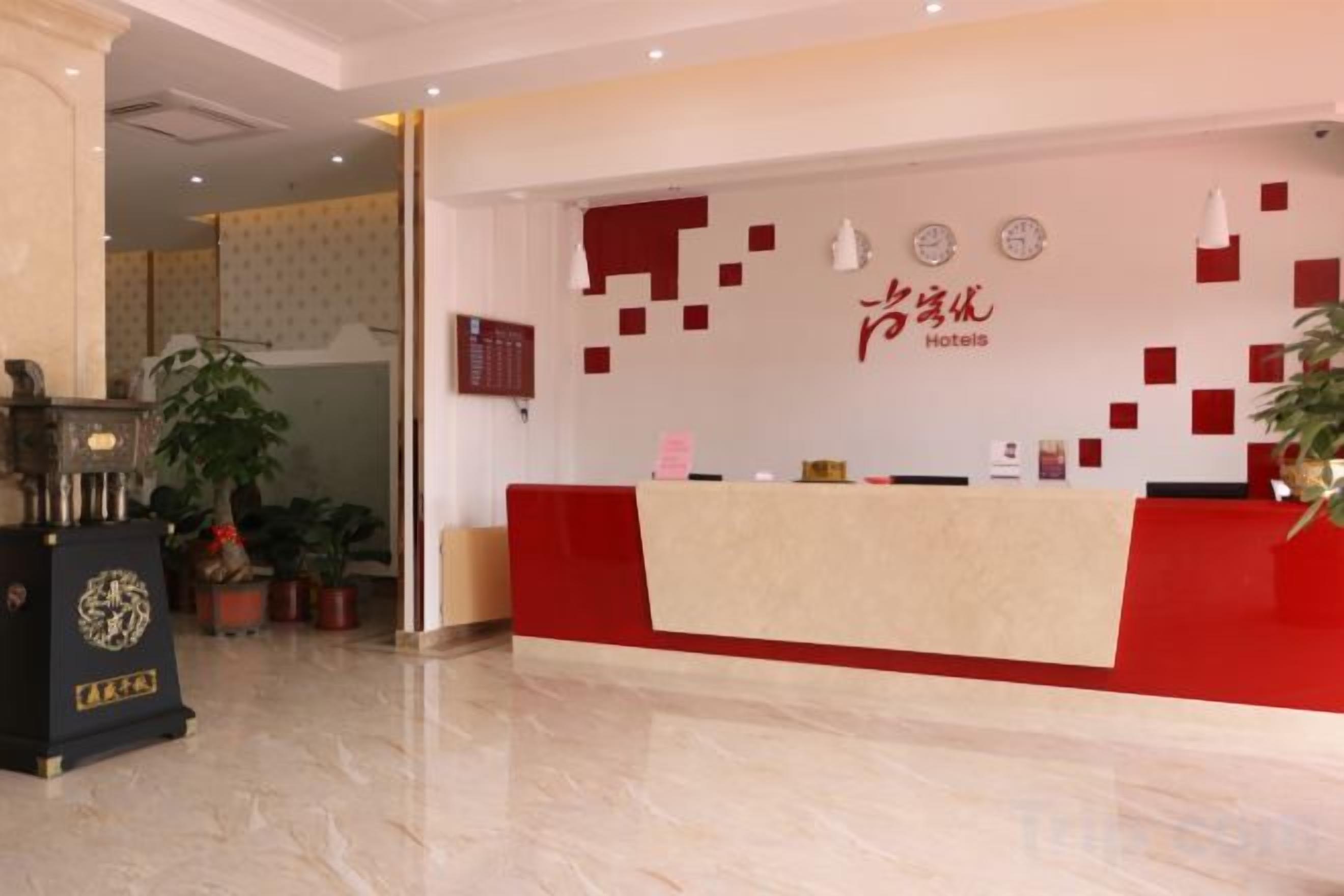 Ein Hotel-Empfangsbereich mit roter Theke, Empfangsschalter und einer Wand mit dem Namen und dem Logo des Hotels.
