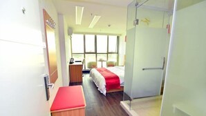 A modern hotel room with a bed, a desk, a chair, a bench, and a glass shower enclosure. - Shankee Express Hotel (Meizhou Lijiangwan) (Meizhou)