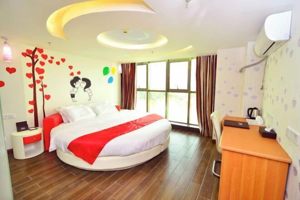 A modern hotel room with a round bed, a desk, and a large window.