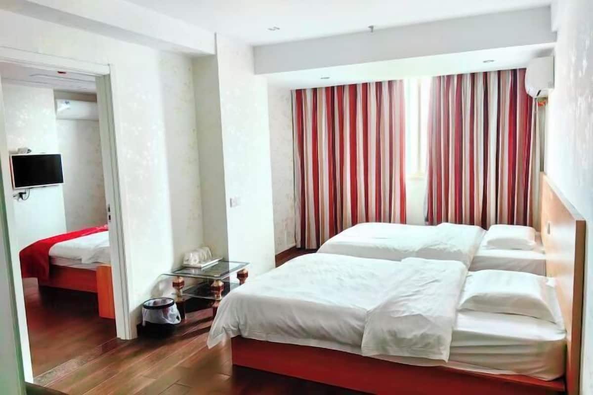 A hotel room with a large bed, a TV, and a separate bed in the adjacent room.