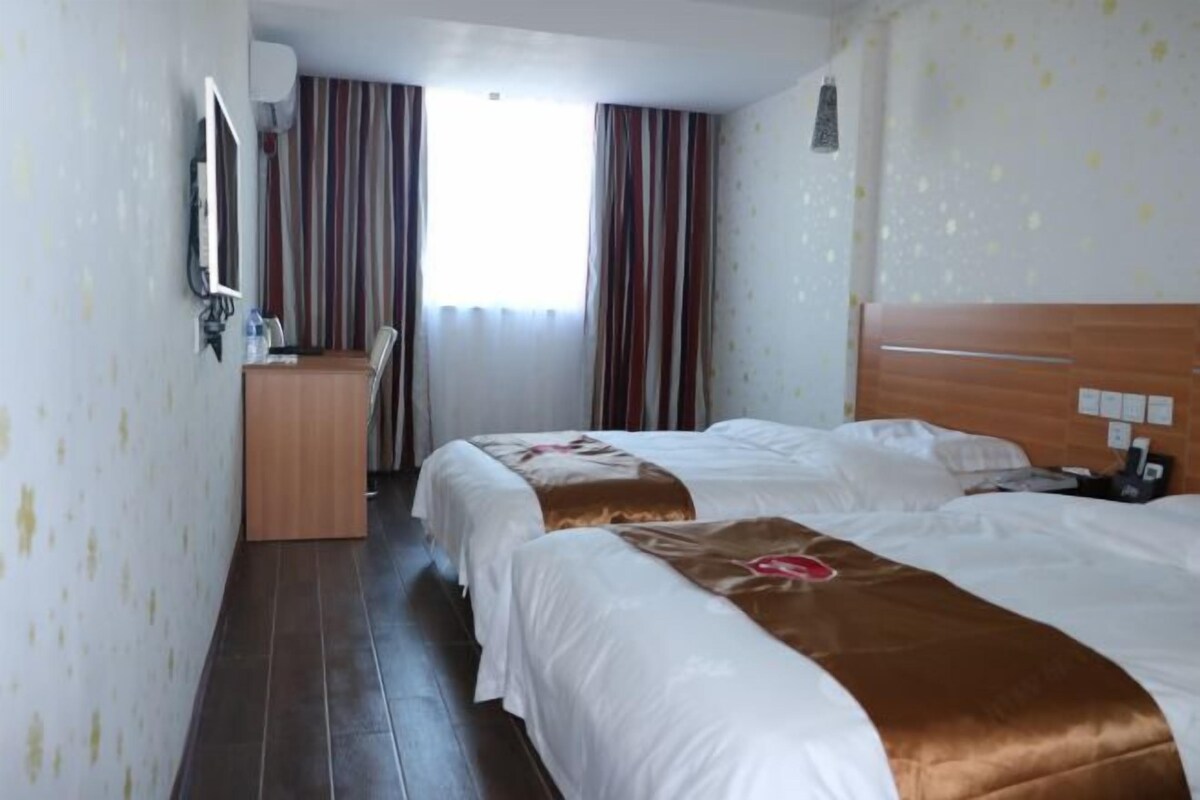 A hotel room with two beds, a desk, a mirror, and a window with curtains.