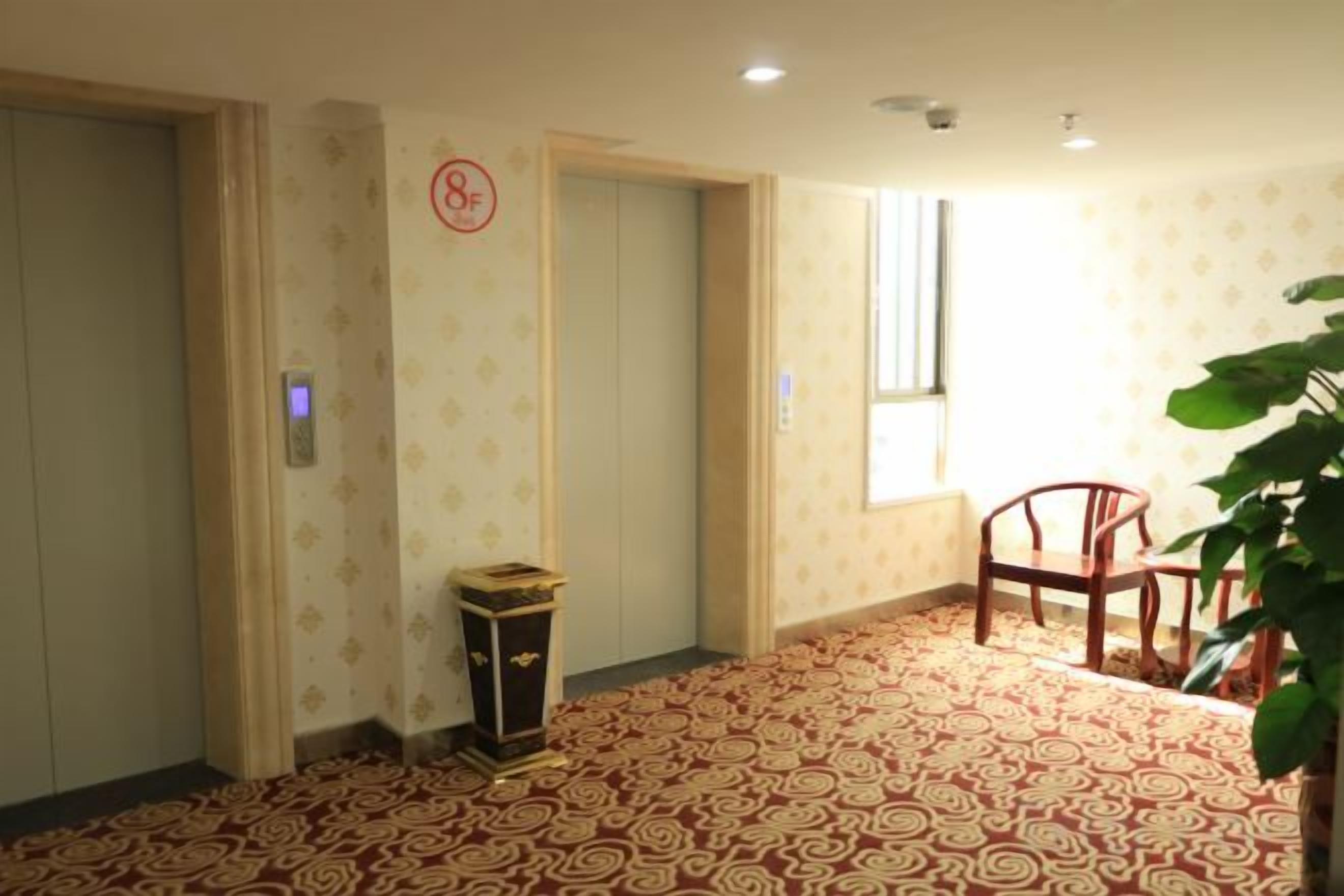 Quarto de hotel com carpete estampado, duas portas, uma mesinha, uma cadeira e uma janela.