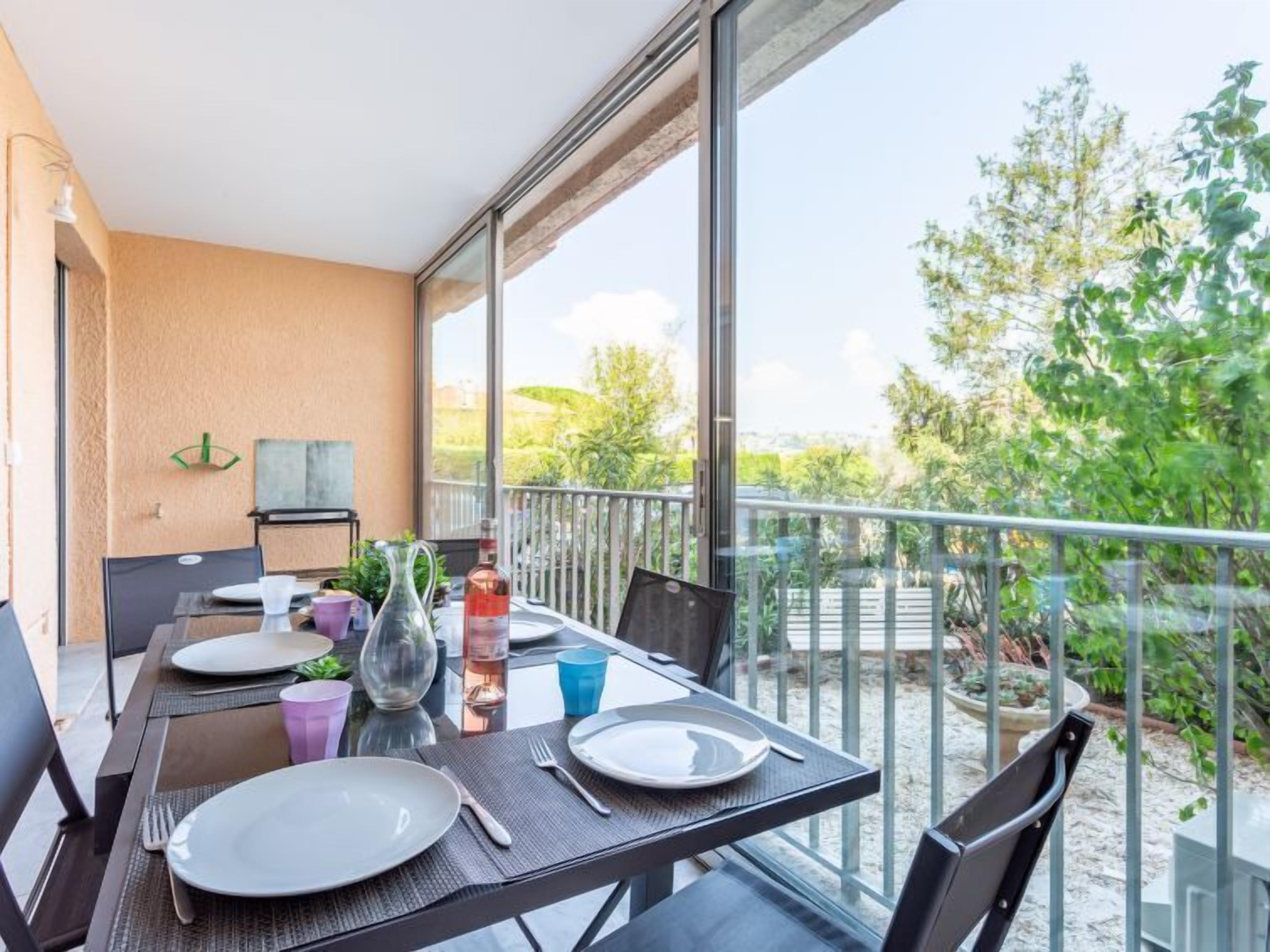 A balcony with a table set for dining, overlooking a garden and trees.