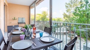 A balcony with a table set for dining, overlooking a garden and trees. - Le Phenicia by Interhome (Saint Laurent du Var)