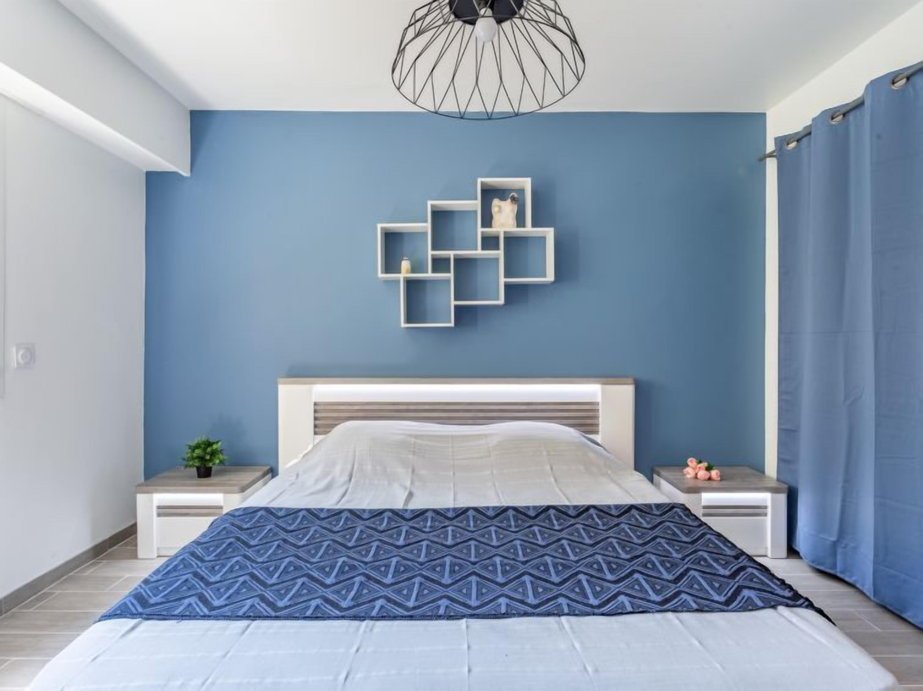 A modern bedroom with a bed, a geometric wall art piece, and a blue curtain.