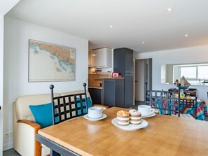 Een moderne woonkamer met een houten eettafel, een bank en een keuken op de achtergrond.