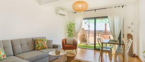Ein modernes Wohnzimmer mit einem grauen Sofa, einem runden Couchtisch und einem Essbereich mit Tisch und Stühlen.