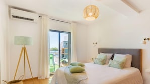 Een slaapkamer met een bed, een staande lamp, een raam en een plafondlamp.