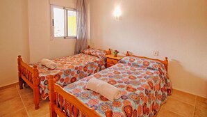 A room with two wooden beds with colorful patterned bedding, a small bedside table with a lamp, and a window with curtains. - Voramar by Interhome (Calpe/Calp)